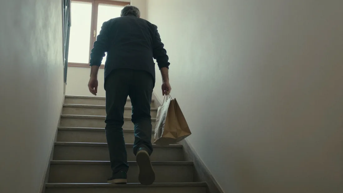Un uomo sale le scale di casa con la spesa in mano, senza toccare il corrimano